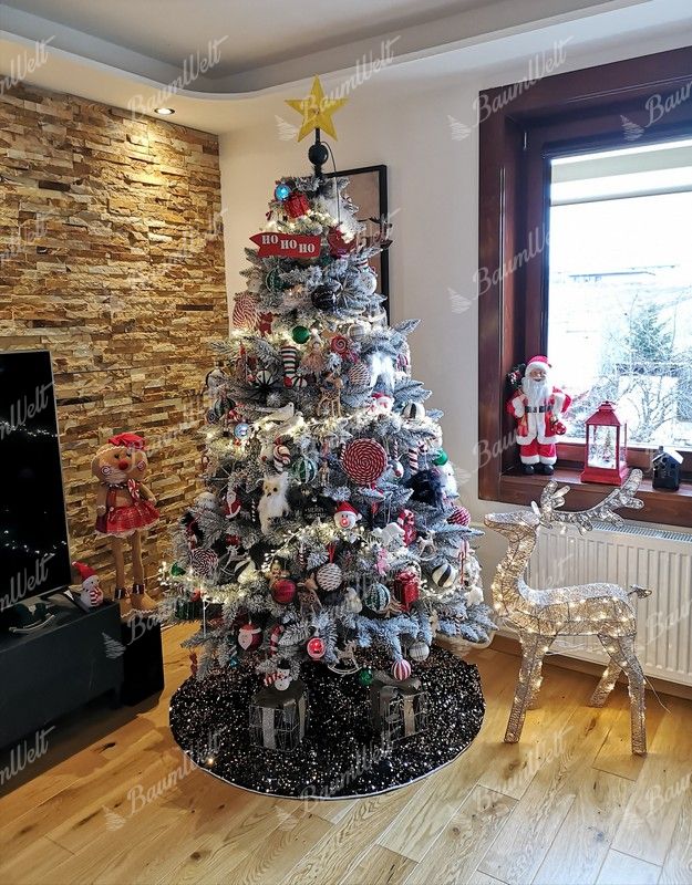 Ein schneebedeckter künstlicher Weihnachtsbaum, geschmückt mit rot-weißen Weihnachtsdekorationen, im Wohnzimmer