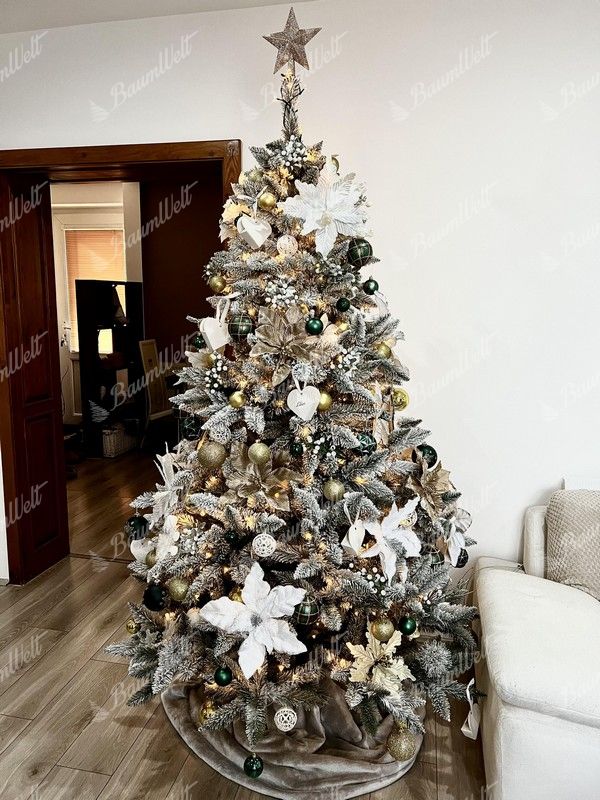 Künstlicher Weihnachtsbaum mit schneebedeckten Zweigen, verziert mit weißen und goldenen Weihnachtsornamenten, mit warmweißer Beleuchtung im Wohnzimmer